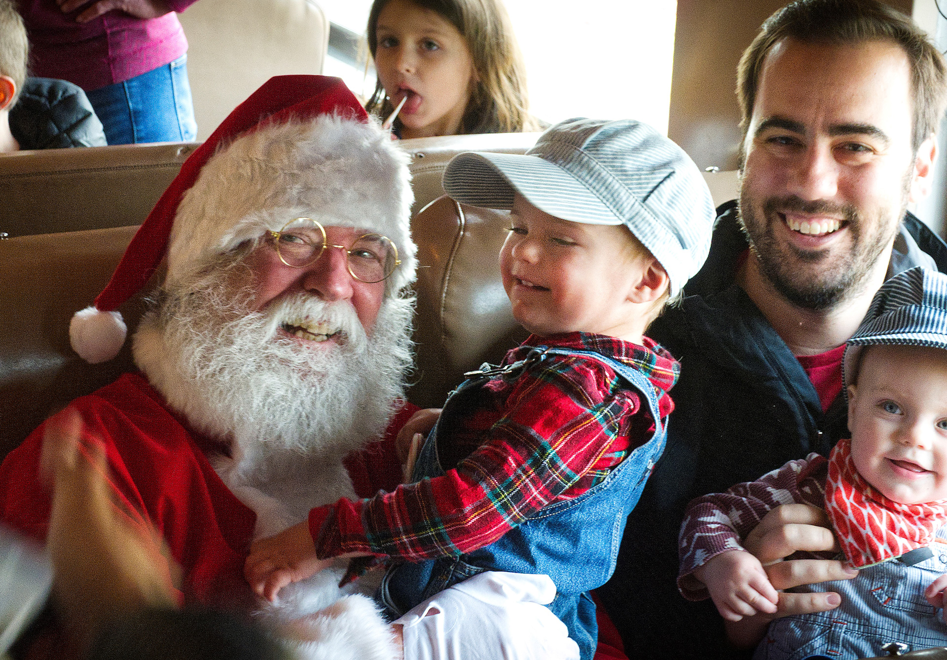 Santa Claus holding a young boy sitting next to a dad holding another young boy on the Holiday Express train